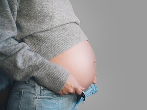 Closeup of pregnant belly with hands on waist of unzipped jeans.