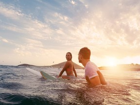 Fit couple surfing at sunset - Surfers friends having fun inside ocean - Extreme sport and vacation concept - Focus on man head - Original sun color tones
