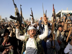 Houthi fighters brandish their weapons during a protest following US and British forces strikes, in the Huthi-controlled capital Sanaa