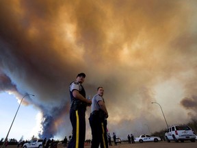 Police officers direct traffic under a cloud of smoke from a wildfire in Fort McMurray, Alta., on Friday, May 6, 2016.