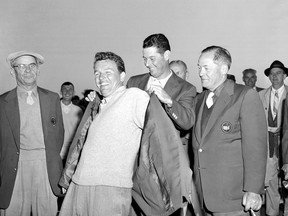 FILE - Jack Burke Jr. is helped by Cary Middlecoff as he puts on the traditional coat after winning the 20th Masters Golf Tournament at the Augusta National Golf Course in Augusta, Ga., April 8, 1956. Jack Burke Jr., the oldest living Masters champion who staged the greatest comeback ever at Augusta National for one of his two majors, died Friday morning, Jan. 19, 2024, in Houston. He was 100. (AP Photo/File)