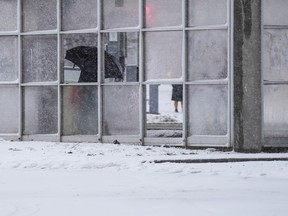 A person huddles in a bus shelter as they wait for public transit as winter storm moves in swathes of Ontario, in Toronto, Tuesday, Jan. 9, 2024.