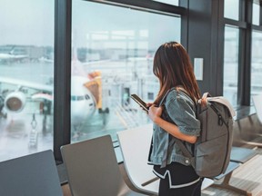A woman uses a smartphone inside an airport while travelling with a backpack.