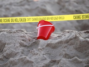 A pail rests next to caution tape on a beach
