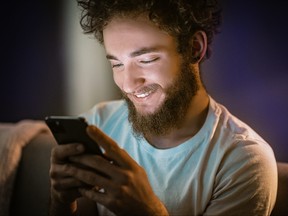 Man with curly hair and beard smiling as he looks at his phone.