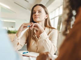 Businesswoman holding pen, sitting in office, looking at colleagues in pensive way.