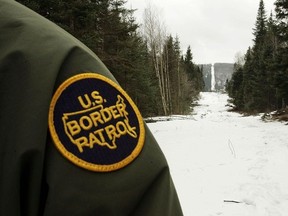 A U.S. Border Patrol agent stands along the boundary marker cut into the forest marking the line between Canadian territory on the right and the United States in Vermont.