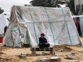 A Palestinian boy sits near a tent for displaced people