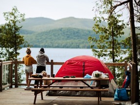 Campers and dog next to red tent looking at Quebec scenery.