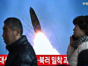 People walk past a television showing a news broadcast with file footage of a North Korean missile test.