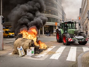 A farmer in a tractor and burning tires block a street