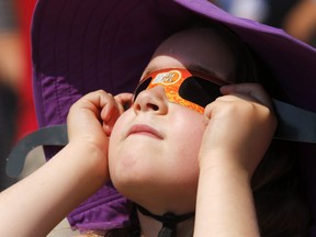 Emily Fee of Belleville views the solar eclipse through viewing glasses Monday, Aug. 21, 2017 in Market Square in Belleville, Ont.