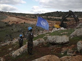 UN peacekeepers hold their flag, as they observe Israeli excavators attempt to destroy tunnels built by Hezbollah, near the southern Lebanese-Israeli border village of Mays al-Jabal, Lebanon on Dec. 13, 2019.