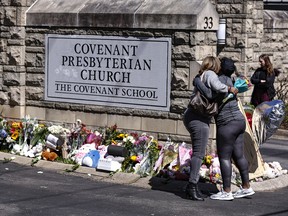 Two women hug near a memorial at the entrance to The Covenant School