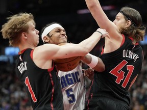 Magic forward Paolo Banchero (centre) tries to drive between Raptors guard Gradey Dick (left) and teammate Kelly Olynyk (right) during second half NBA action in Toronto, Friday, March 15, 2024.