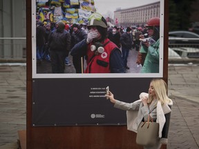 A woman walks holding her mobile phone past a photograph showing a scene from the 2014 Maidan revolution in Kyiv, Ukraine, Thursday, March 14, 2024.