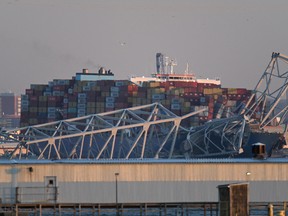The steel frame of the Francis Scott Key Bridge sits on top of a container ship