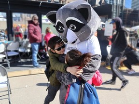 Two children hugging Celebrate Torontos mascot, Remi the Raccoon.