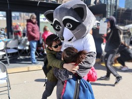 Two children hugging Celebrate Torontos mascot, Remi the Raccoon.