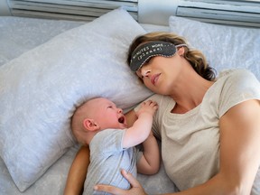 A tired mother tries to take a nap while a baby cries next to her in bed.
