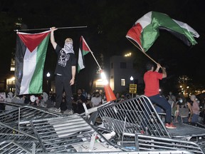 George Washington University students, protesting the Israel-Hamas war, stand on top of police barricades as they celebrate breaking through the fencing, in Washington, Monday, April 29, 2024. (AP Photo/Cliff Owen)
