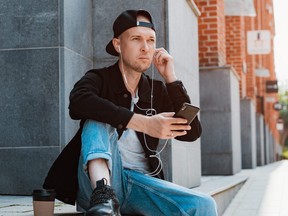 Guy in a black cap holding smartphone and wearing headphones.