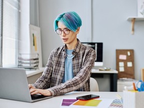 Creative young man with blue hair using laptop in office