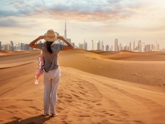 A tourist woman stands in the Red Desert and looks at the distant skyline of Dubai, United Arab Emirates.