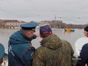 In this grab taken from a video released by the Russian Emergency Ministry Press Service on Sunday, April 7, 2024, Russian Emergency Situations Minister Alexnader Kurenkov, center left, back to a camera, stands on a boat observing water levels, in Orsk, Russia.
