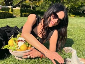 Actress Abigail Spencer playing with dog on grass with basket of jam and lemons nestled in front of her.