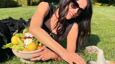 Actress Abigail Spencer playing with dog on grass with basket of jam and lemons nestled in front of her.