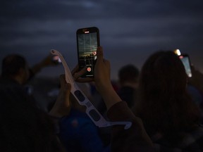 Canada's two largest mobile carriers say bolstered capacity helped their networks handle the extra wireless traffic in hot spot regions where tens of thousands gathered to take in Monday's total solar eclipse. People use their phones to document the total solar eclipse in Niagara Falls, Ont., on Monday, April 8, 2024.