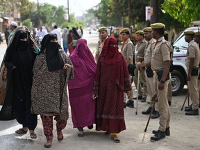 Police stand guard as voters arrive amid to cast their ballots at a polling station during the first phase of India's general election in Kairana, Uttar Pradesh state, on April 19, 2024.