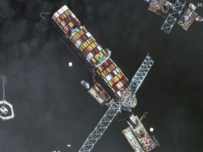 This satellite image provided by Maxar shows the bow of the container ship Dali remains stuck underneath sections of the fallen Francis Scott Key Bridge, while salvage crews and barges with cranes continue removing some of the bridge debris and hundreds of shipping containers still onboard the vessel, in Baltimore, Monday, April 8, 2024.