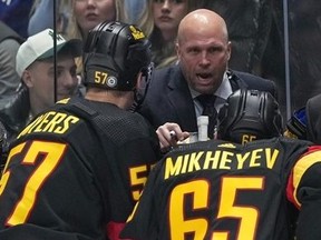 Vancouver Canucks head coach Rick Tocchet, back centre, and assistant coach Adam Foote, back right, listen as assistant coach Mike Yeo, back left, talks to players.