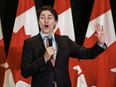 Justin Trudeau speaks and gestures with Canadian flags in the background