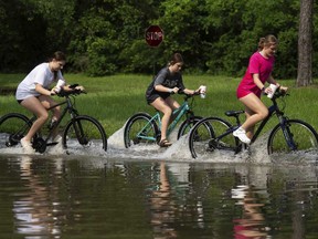 Girls ride their bikes through flood water near the bridge over Lake Houston along West Lake Houston Parkway after it was closed due to high water on either side of the thoroughfare, Saturday, May 4, 2024, in Kingwood, Texas.