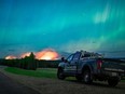 The Aurora Borealis shines overhead of a B.C. Conservation Officer Service vehicle near the junction of highways 97 and 77, as a wildfire burns in the background near Fort Nelson, B.C., in a Saturday, May 11, 2024, handout photo.