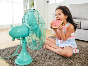 A child cools off eating watermelon in front of a fan.