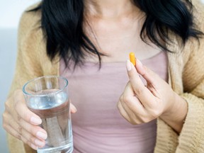 woman hand taking turmeric pill, girl hand holding turmeric powder in capsule or curcumin herb medicine with a glass of water
