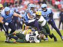 Toronto Argonauts running back Ka'Deem Carey (25) runs the ball against Edmonton Elks defensive lineman Sam Acheampong, right, and defensive back Devodric Bynum (16) during first half CFL football action in Toronto on June 22, 2024.