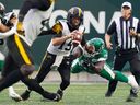 Saskatchewan Roughriders defensive lineman Charbel Dabire (99) tackles Hamilton Tiger-Cats quarterback Bo Levi Mitchell (19) during the first half of CFL football action in Regina, on Sunday, June 23, 2024.
