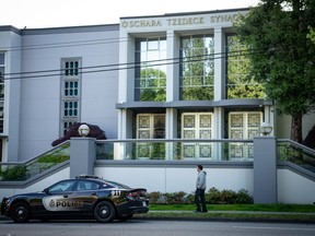 A man walks past as a Vancouver Police Department patrol car sits in front of the Schara Tzedeck synagogue, in Vancouver, B.C., Friday, May. 31, 2024.