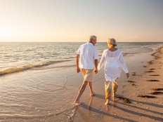 Vacationing couple holds hands on a beach at sunset.