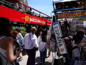 Tourists walk past a souvenir shop and a tourist bus next to Sagrada Familia basilica in Barcelona on April 13, 2024.
