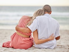 Couple on a beach hug watching the sunset, beach waves and sea together.