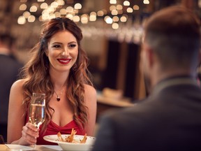 A woman smiles at an unseen man while having dinner in a nice restaurant.