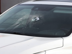 A bullet hole is seen through the front window of an SUV.