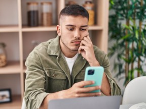 Young man sitting on table using smartphone at home.