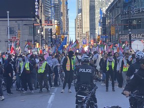 Toronto Police officers watch as protesters march through the intersection of Yonge and Dundas Sts. in downtown Toronto, Saturday, Oct. 5, 2024.
